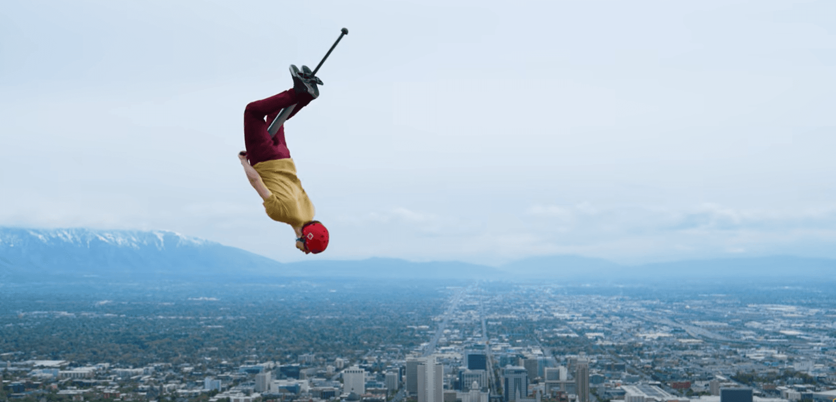 A pogo-stick acrobat mid-flip, high above a city skyline